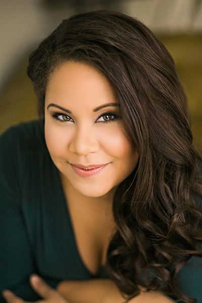 A headshot of singer Ariana Wehr in which she wears a black top and has long brown hair swept over one shoulder.