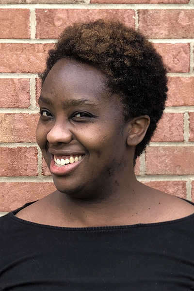 A headshot of Dana Scott, who smiles while wearing a black top in front of a red brick wall.