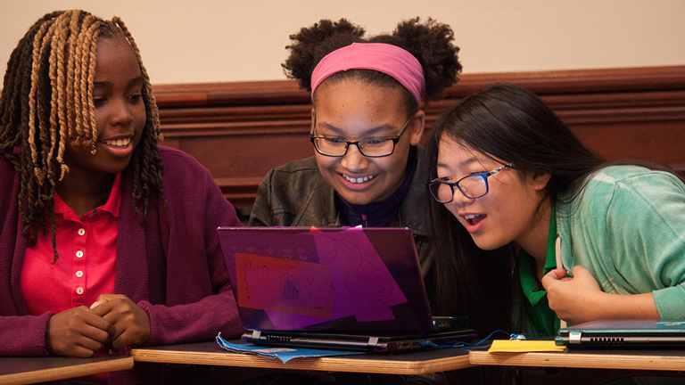 Three young people smiling and looking at a laptop computer screen